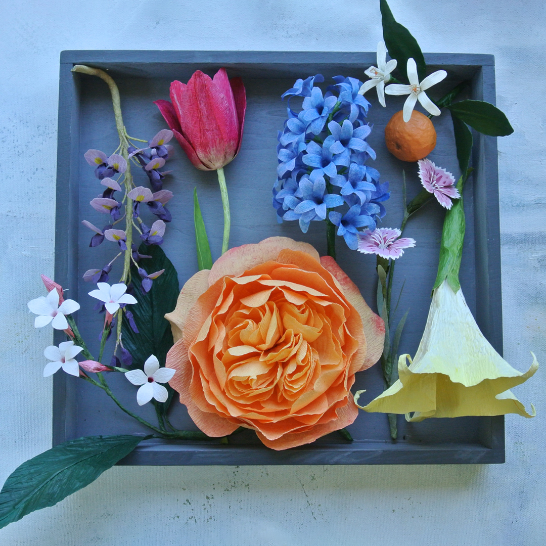 Multi coloured handmade flowers organised neatly in a grey shallow box